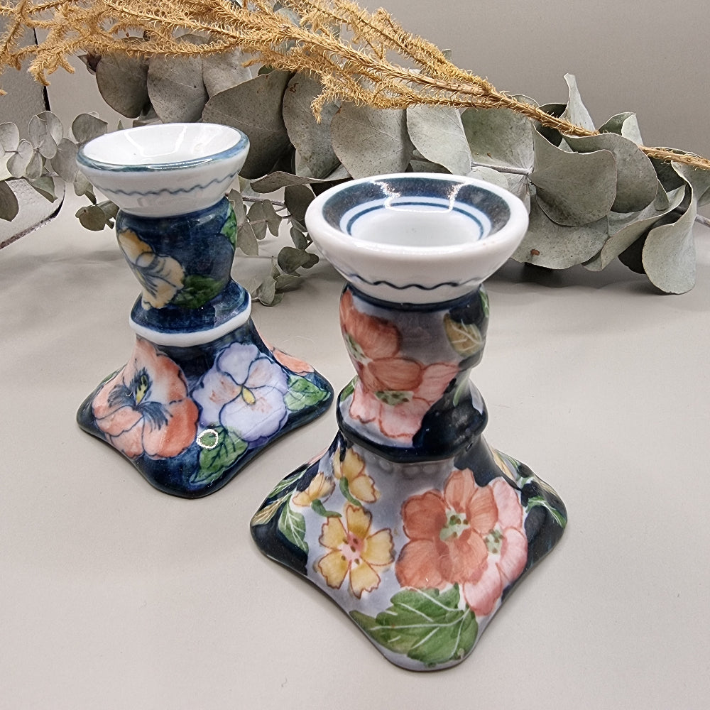 Pair of vintage hand-painted ceramic candlestick holders with pink peach and yellow floral design on navy blue glaze