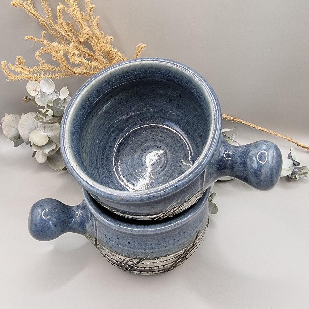 Two rustic blue soup bowls with handles and textured banding.