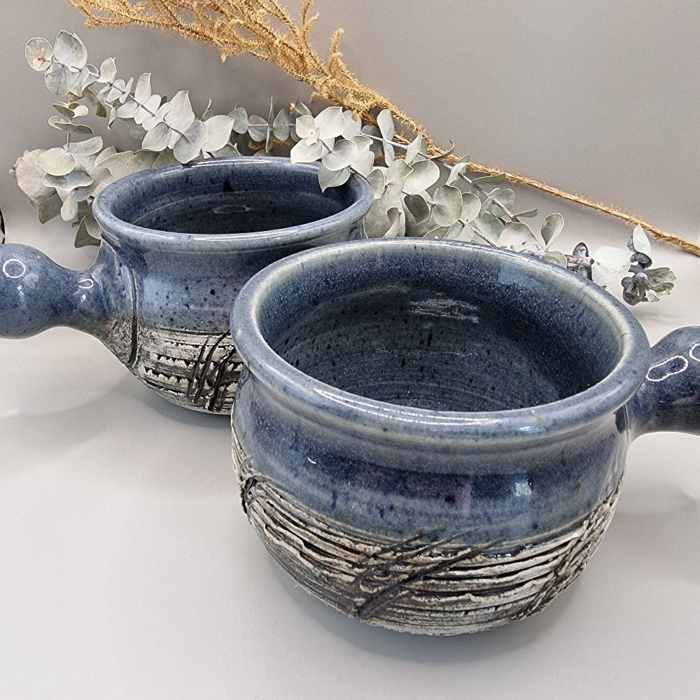 Two rustic blue soup bowls with handles and textured banding.