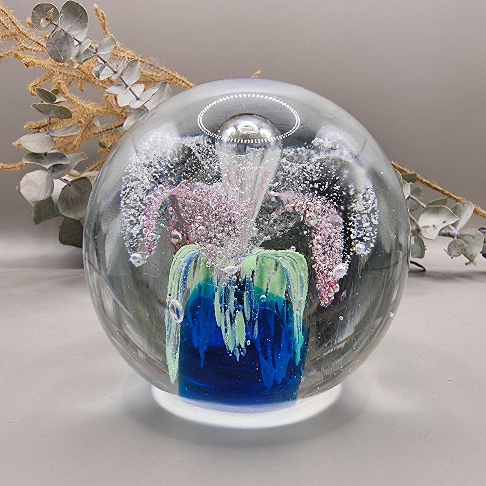 Glass paperweight with pink, blue and green floral swirl and bubble details inside.