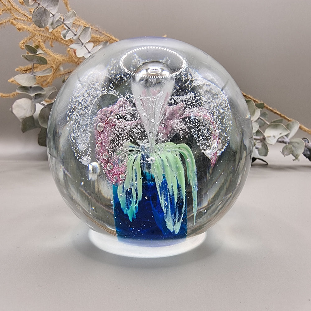 Glass paperweight with pink, blue and green floral swirl and bubble details inside.