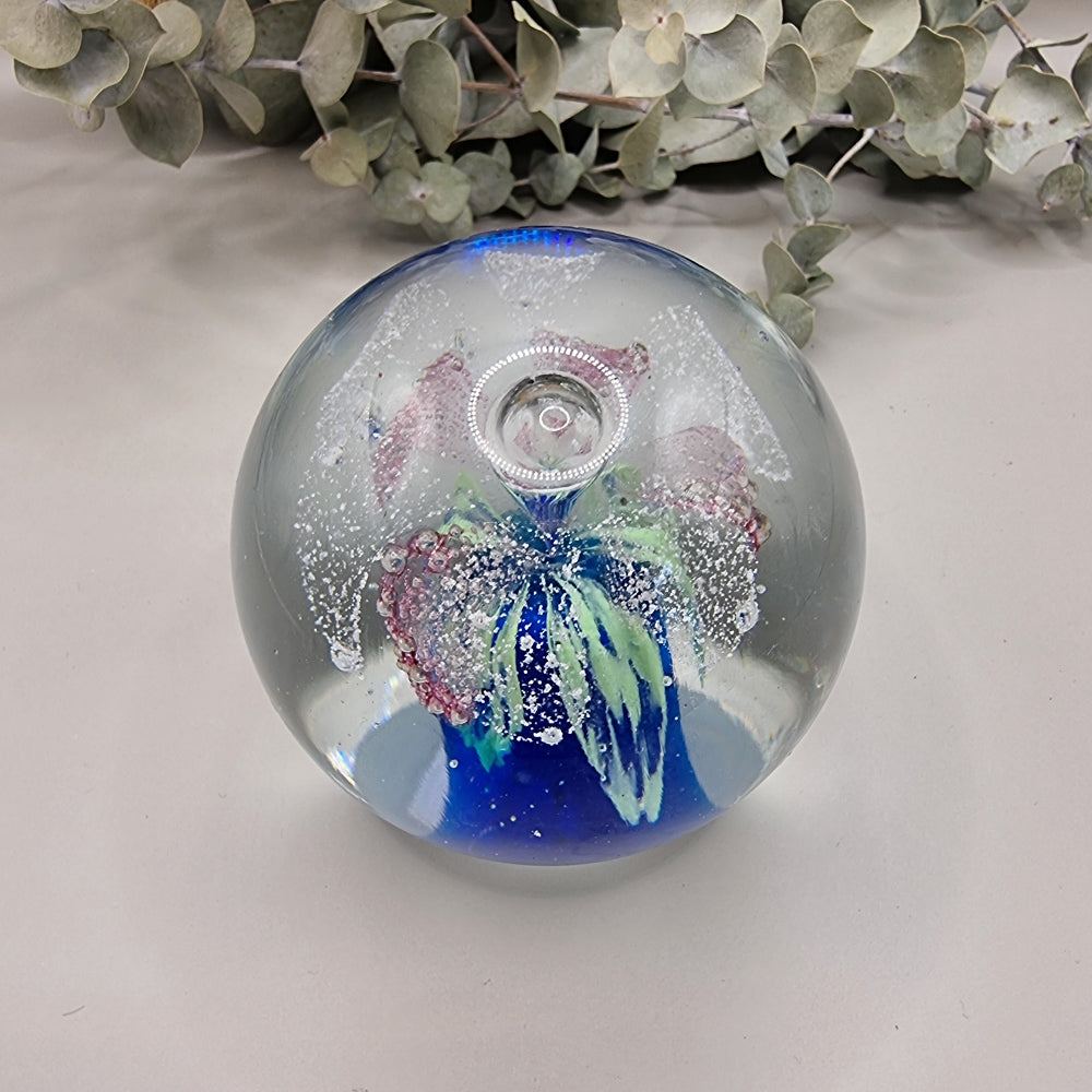Glass paperweight with pink, blue and green floral swirl and bubble details inside.