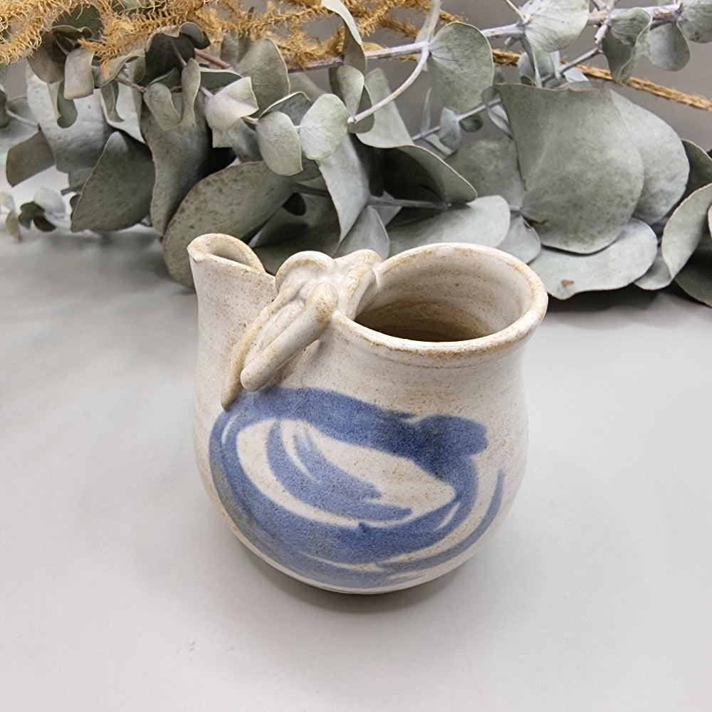 Handmade blue and white ceramic jug with bow detail and painted swirl pattern.