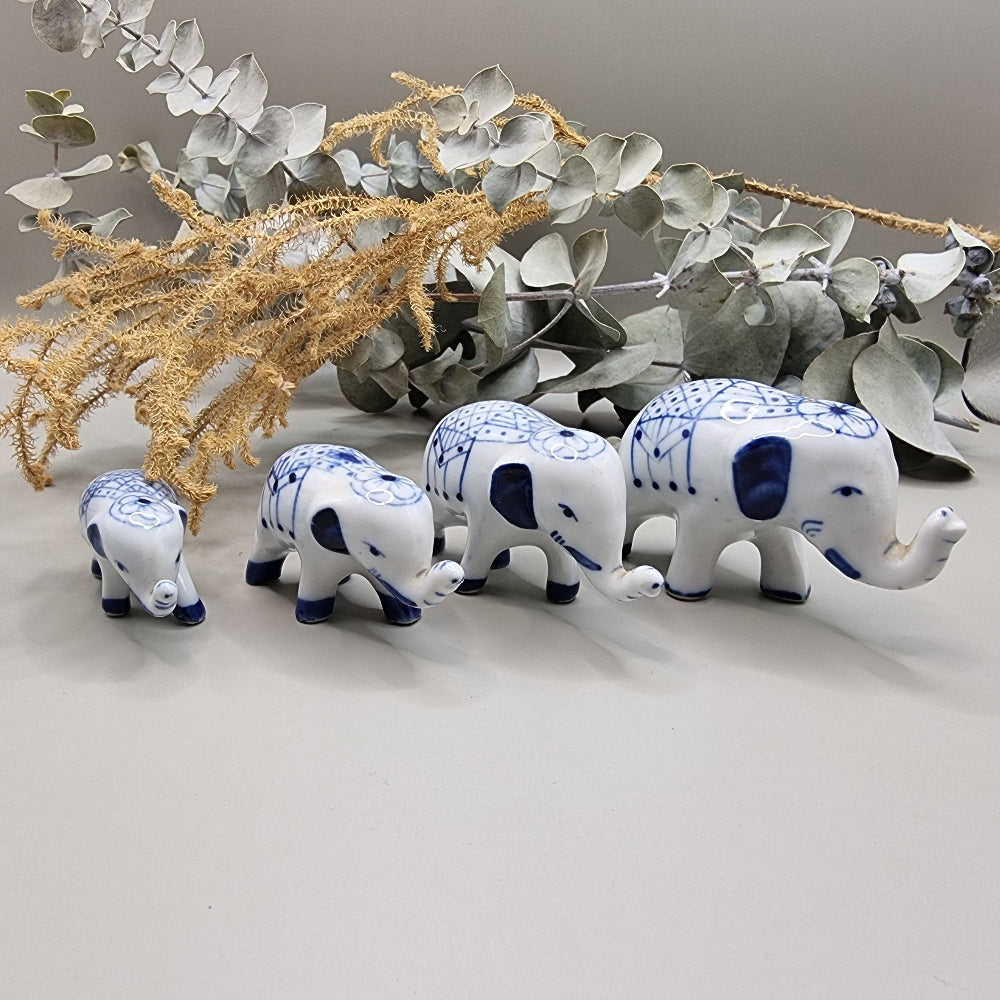 Set of 4 miniature blue and white porcelain elephants with raised trunks and painted blankets.