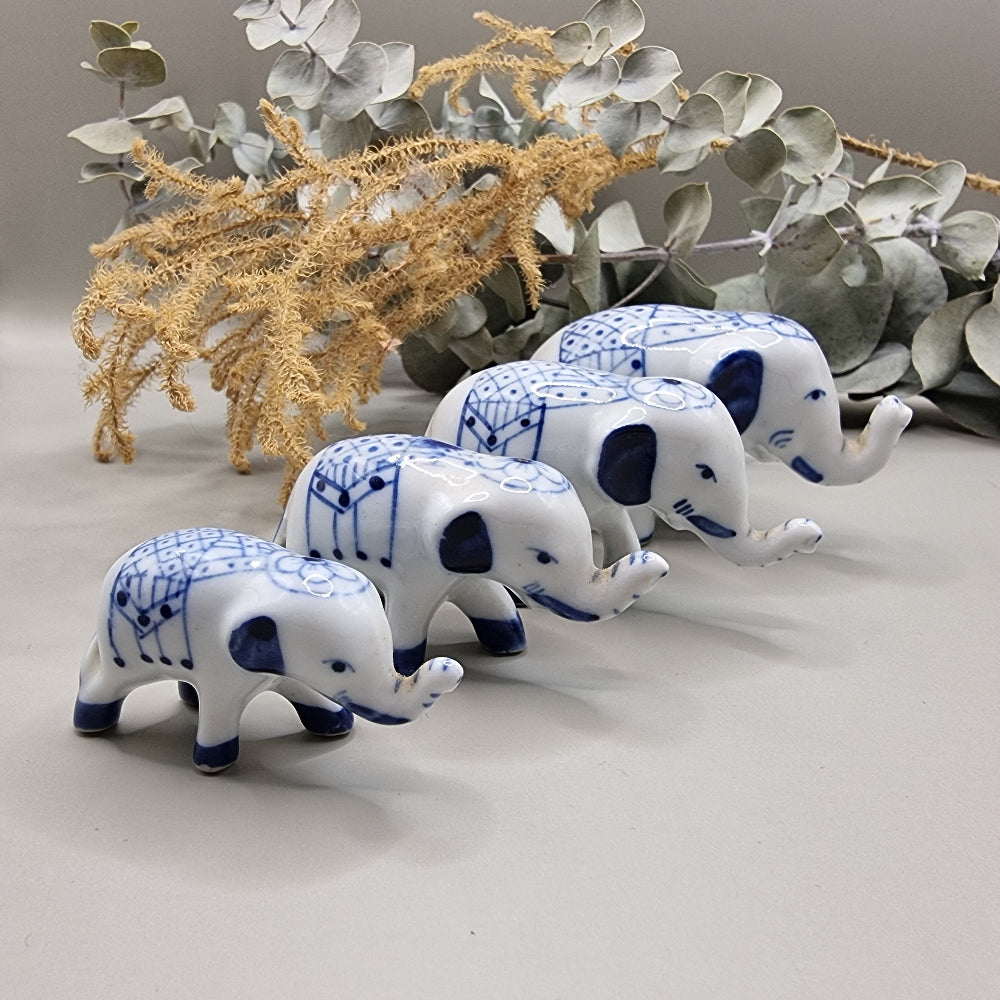 Set of 4 miniature blue and white porcelain elephants with raised trunks and painted blankets.