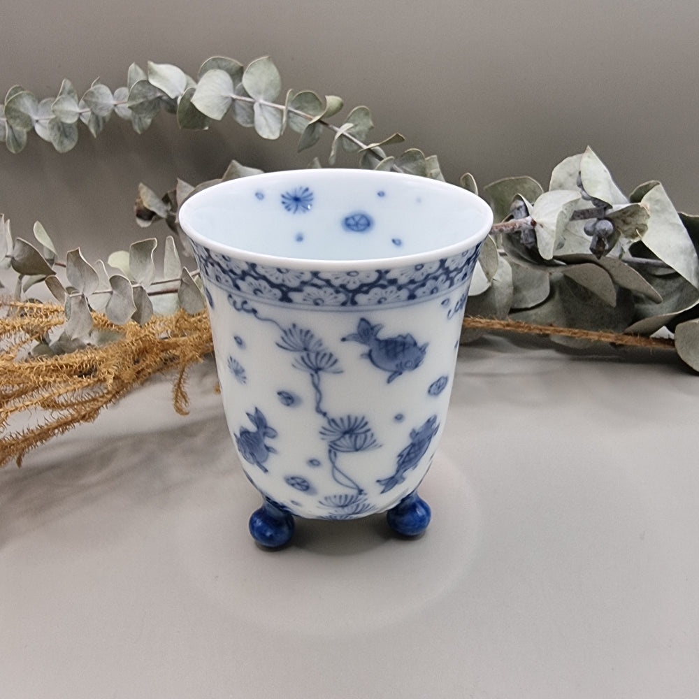 Footed Japanese porcelain sake cup with blue and white goldfish and lotus design.