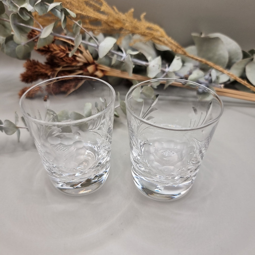 Pair of cut crystal shot glasses with etched floral and leaf pattern.