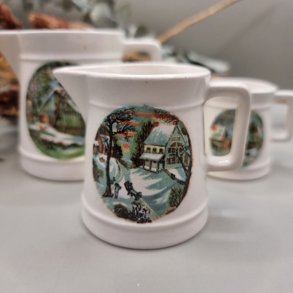 Three white ceramic measuring jugs with colourful winter countryside scenes.