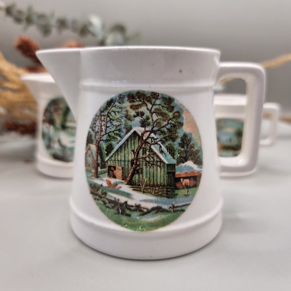 Three white ceramic measuring jugs with colourful winter countryside scenes.