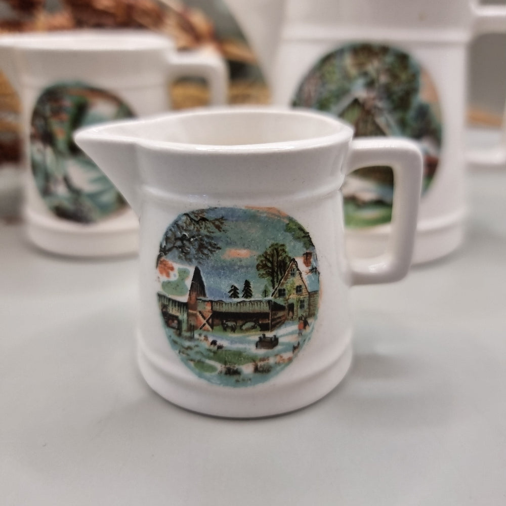 Three white ceramic measuring jugs with colourful winter countryside scenes.
