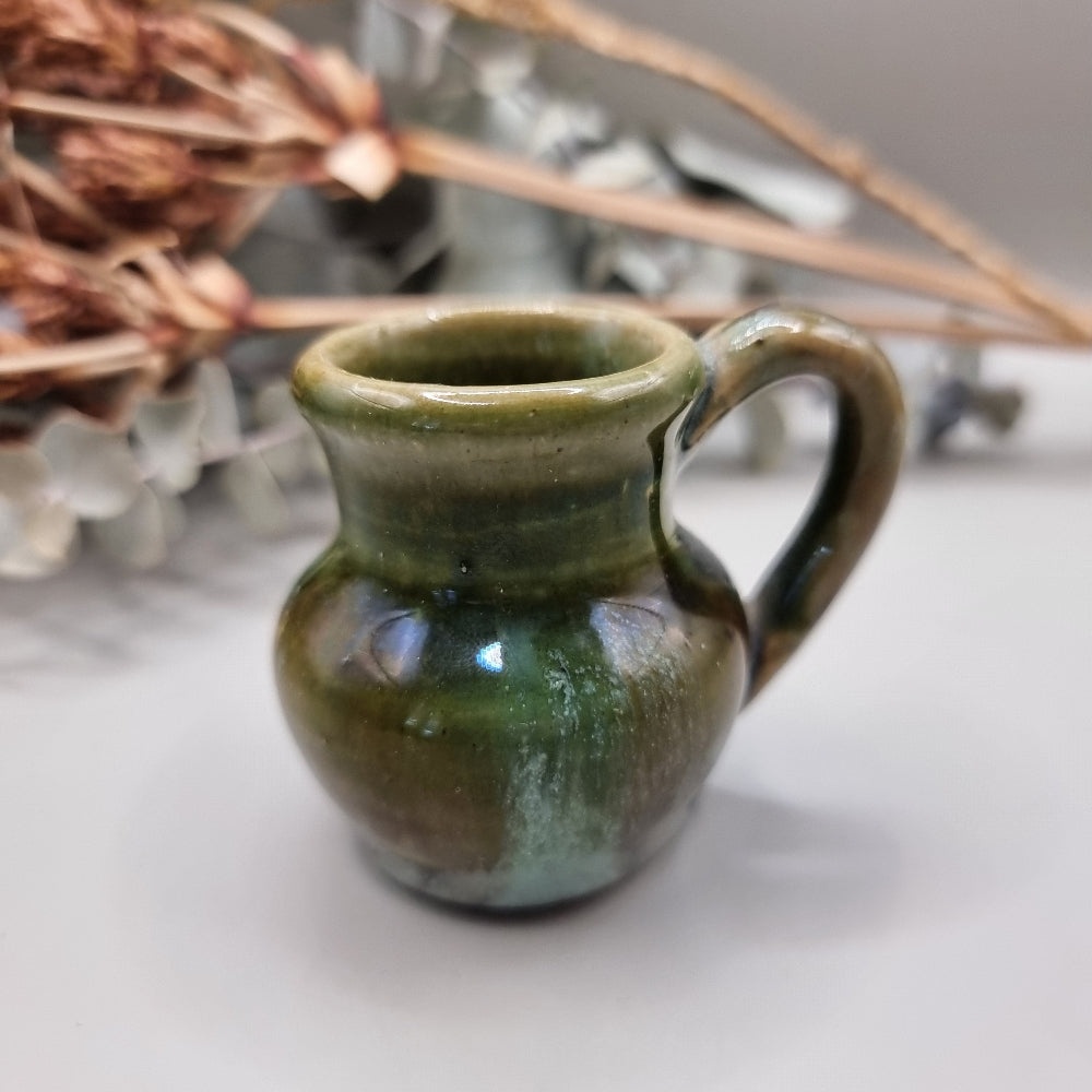 Small green glazed studio pottery jug with rounded shape and handle.