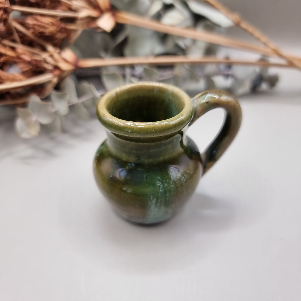 Small green glazed studio pottery jug with rounded shape and handle.