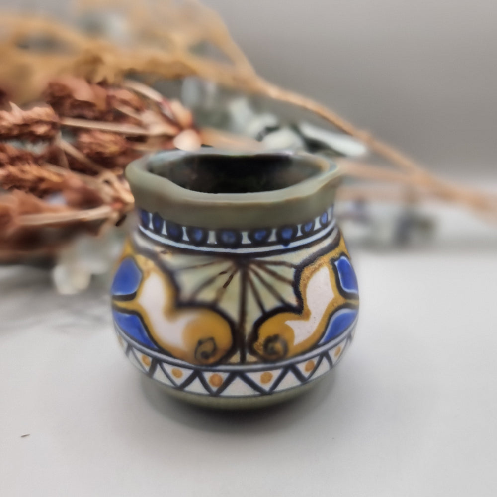 Small hand-painted ceramic pot with blue, gold, and green decorative pattern.