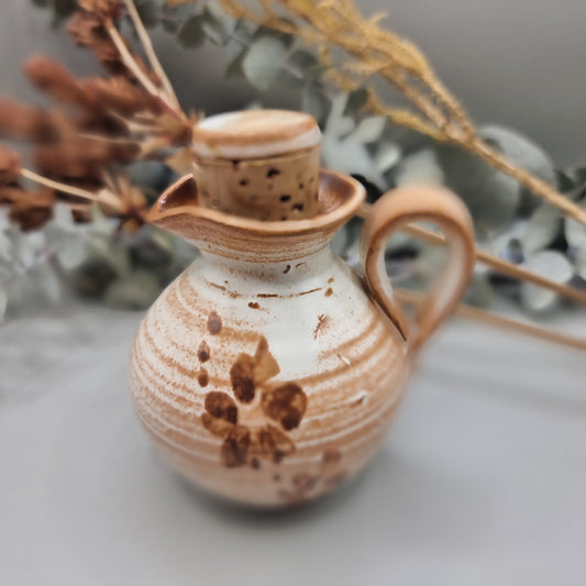 Small handmade pottery jug with earthy orange glaze, floral detail, and lid.