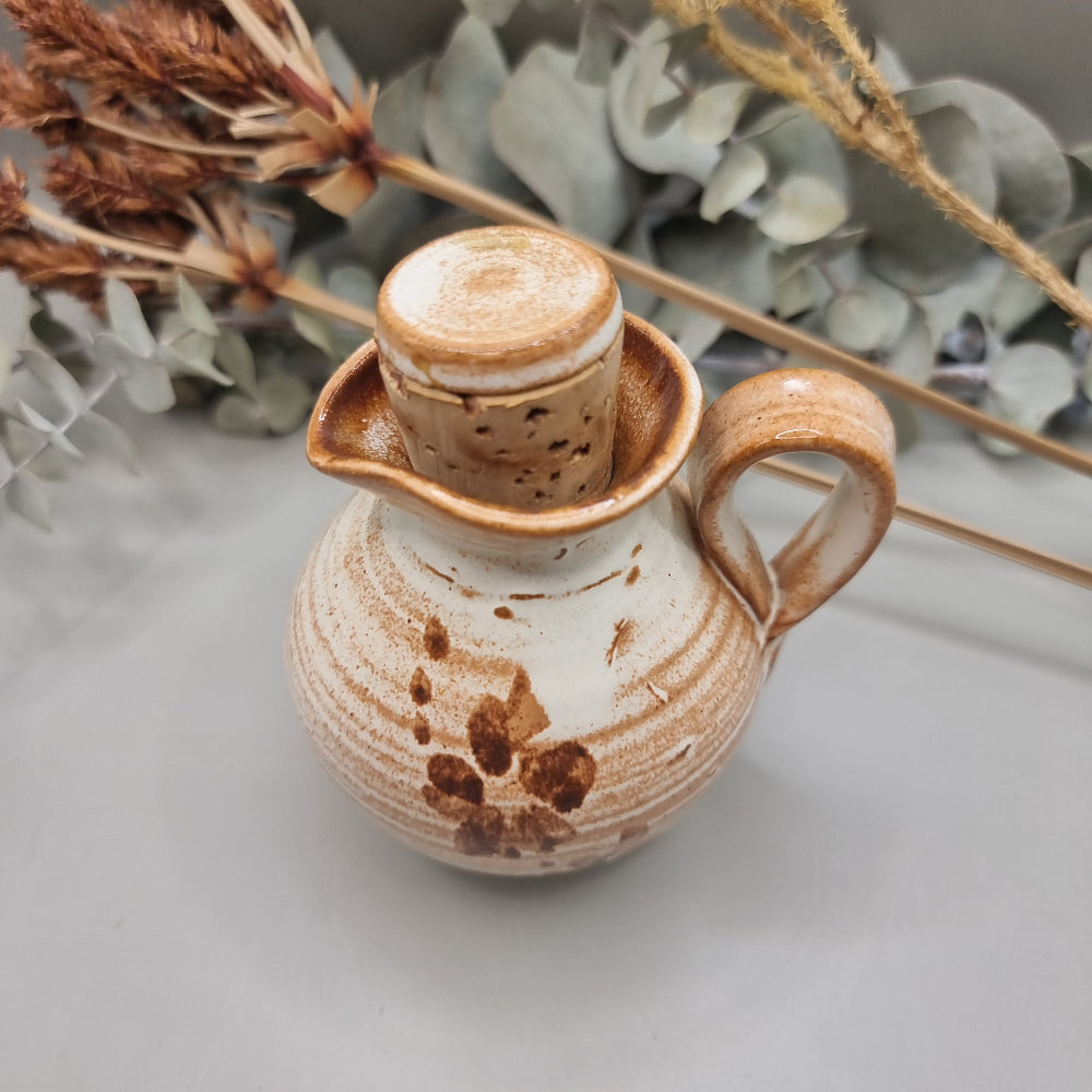 Small handmade pottery jug with earthy orange glaze, floral detail, and lid.