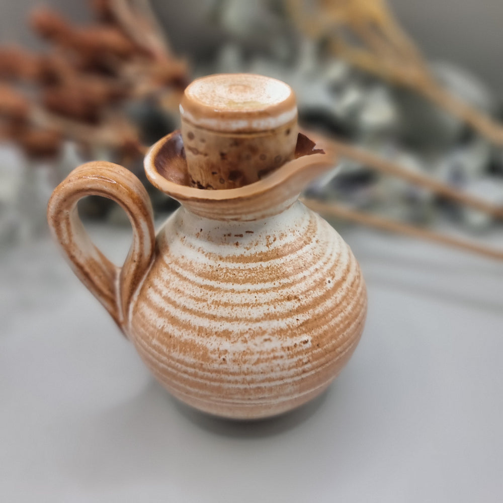 Small handmade pottery jug with earthy orange glaze, floral detail, and lid.