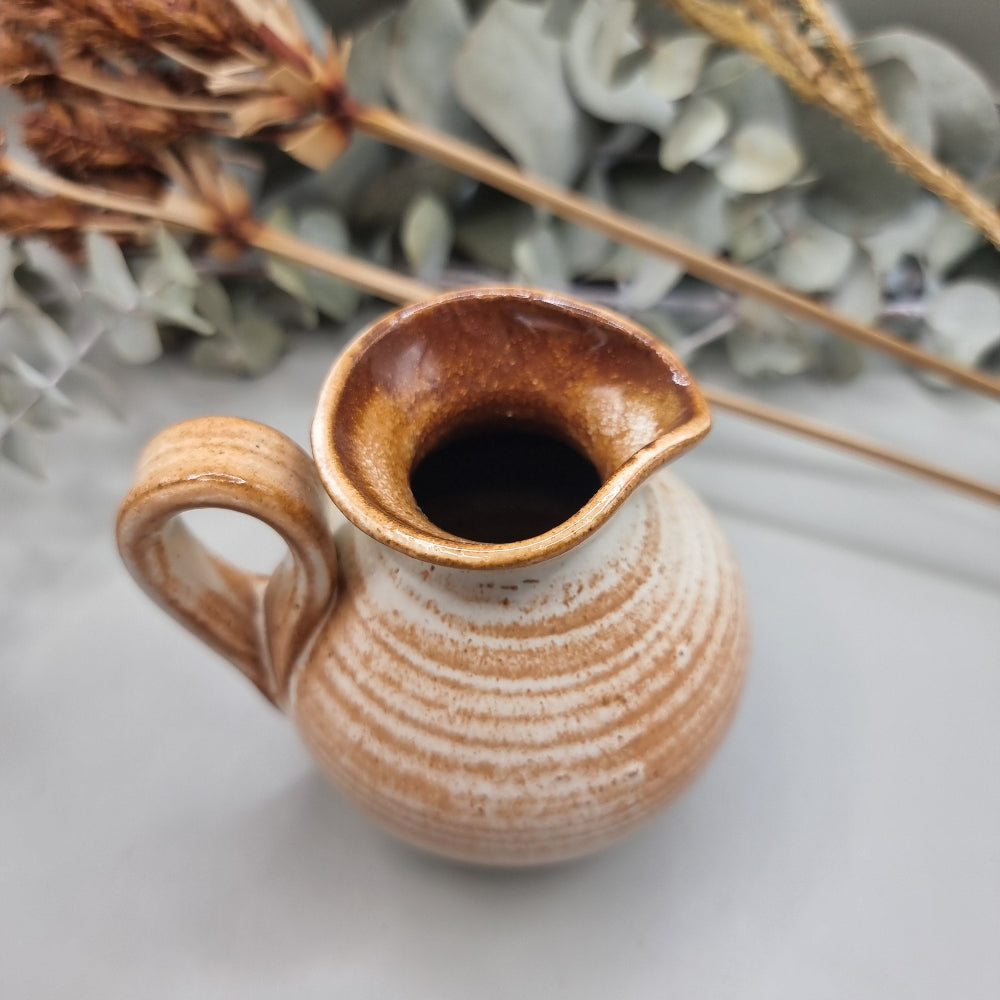 Small handmade pottery jug with earthy orange glaze, floral detail, and lid.