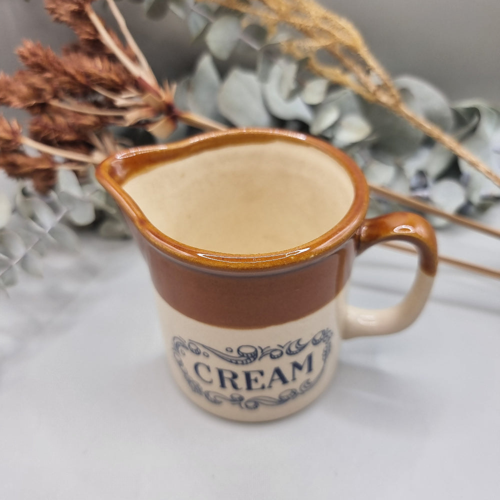 Small vintage stoneware cream jug with brown glaze and “CREAM” in blue lettering.