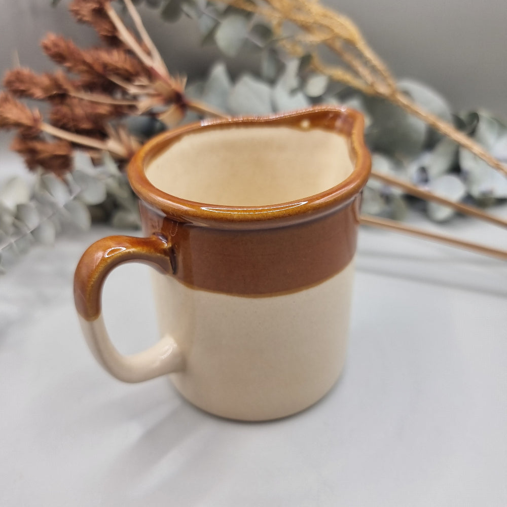 Small vintage stoneware cream jug with brown glaze and “CREAM” in blue lettering.