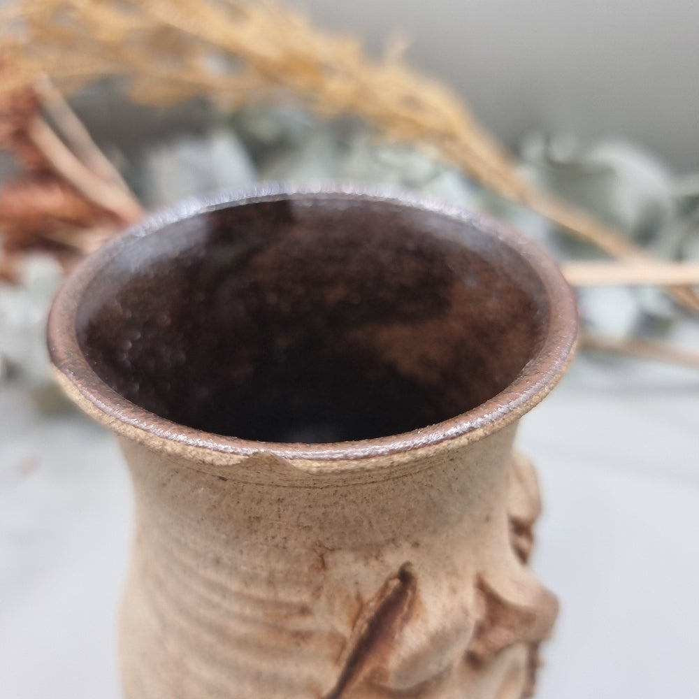 Stoneware face mug with grumpy sculpted expression and rustic brown glaze.