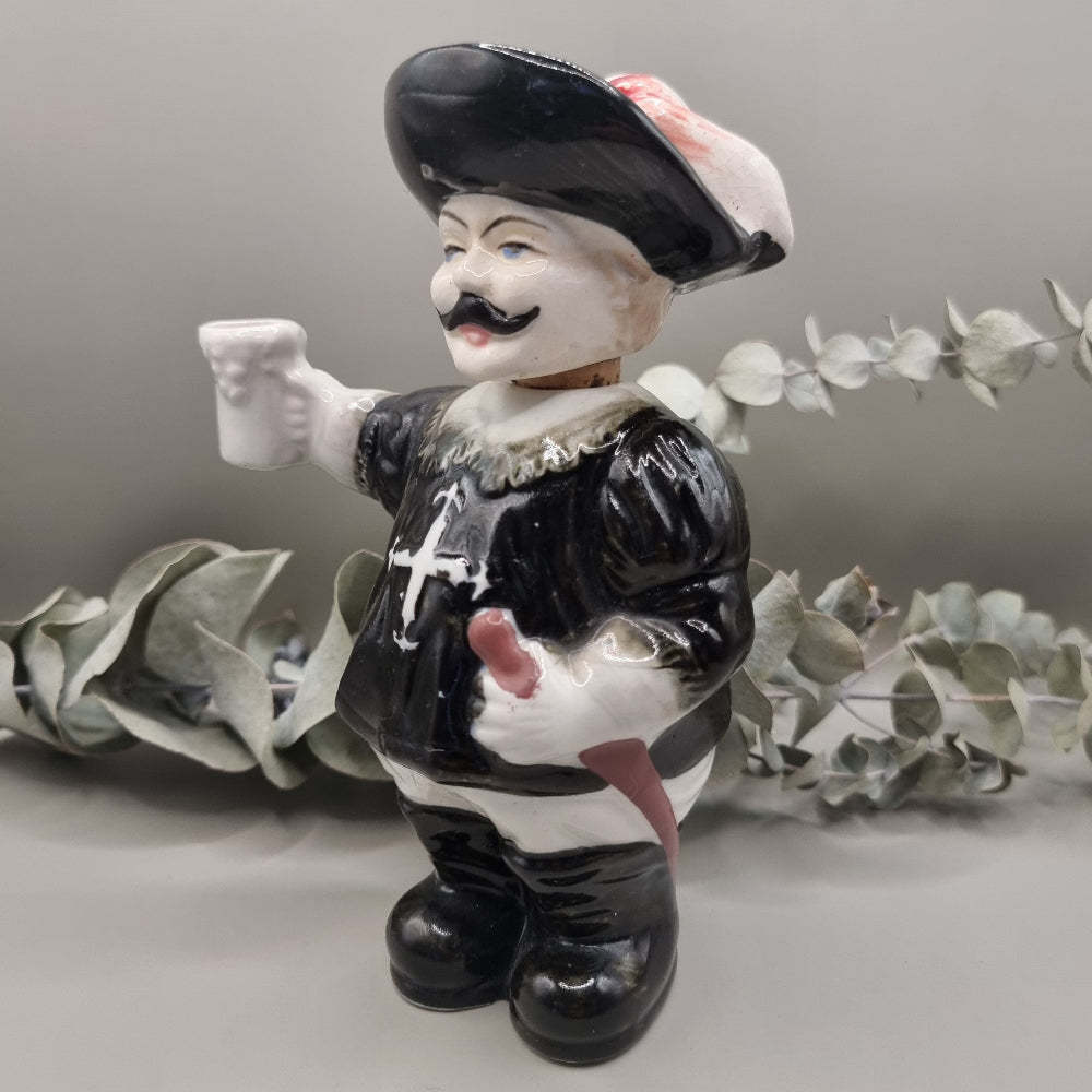 Vintage ceramic musketeer decanter holding a sword and stein with cork stopper and feathered hat.