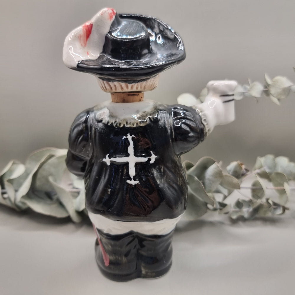 Vintage ceramic musketeer decanter holding a sword and stein with cork stopper and feathered hat.