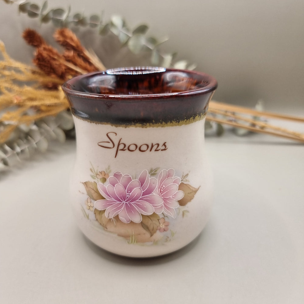 Ceramic spoon holder with pink floral design and brown glazed rim.