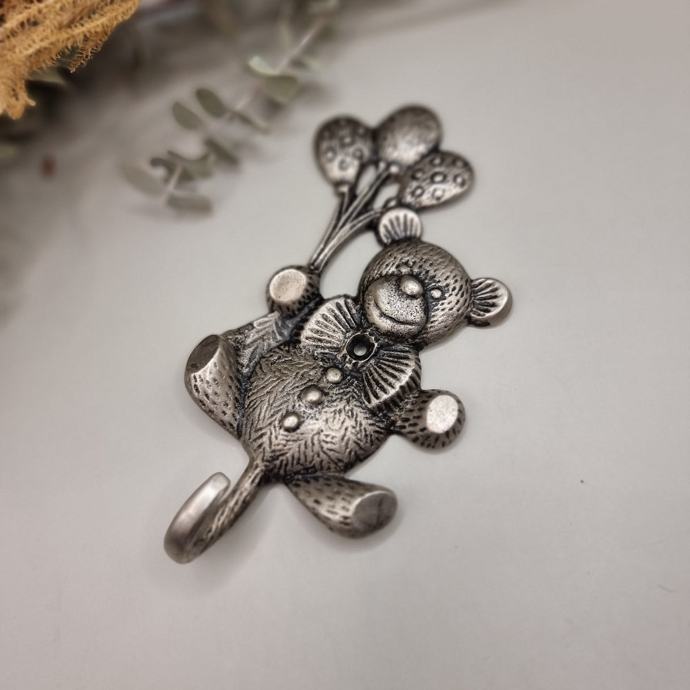 Silver-tone teddy bear wall hook holding balloons with a curved tail hook for hanging items.
