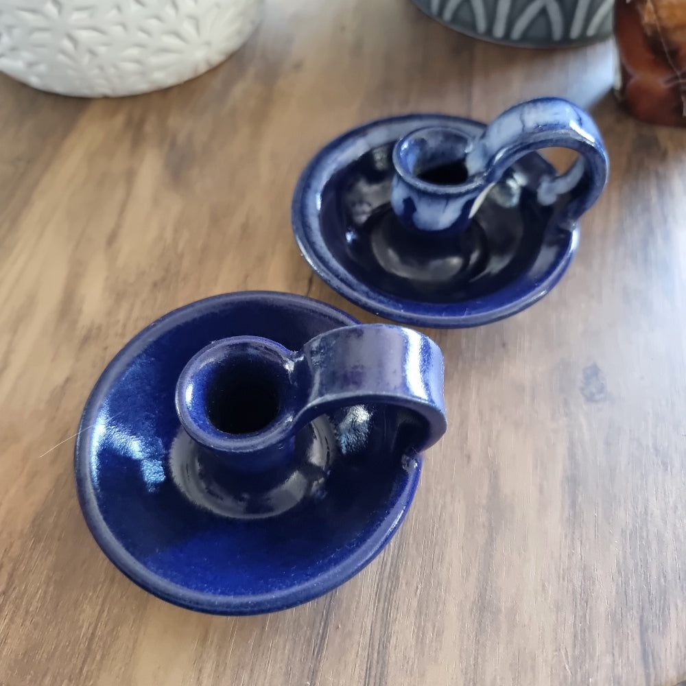 Pair of cobalt blue ceramic chamberstick candle holders with finger loops on a wooden table