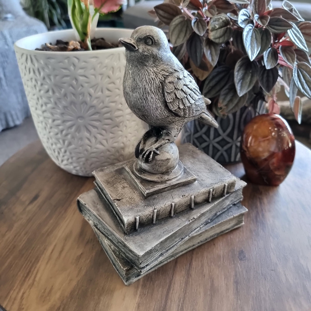 Rustic bird figurine perched on a stack of vintage-style books with a weathered stone finish