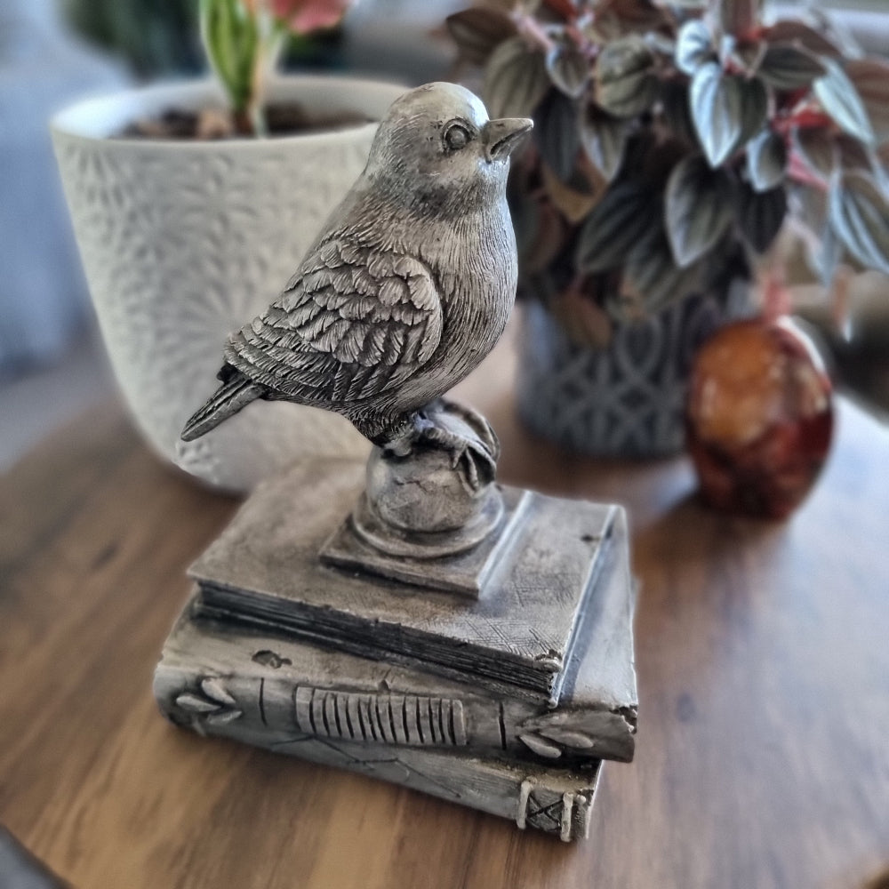 Rustic bird figurine perched on a stack of vintage-style books with a weathered stone finish