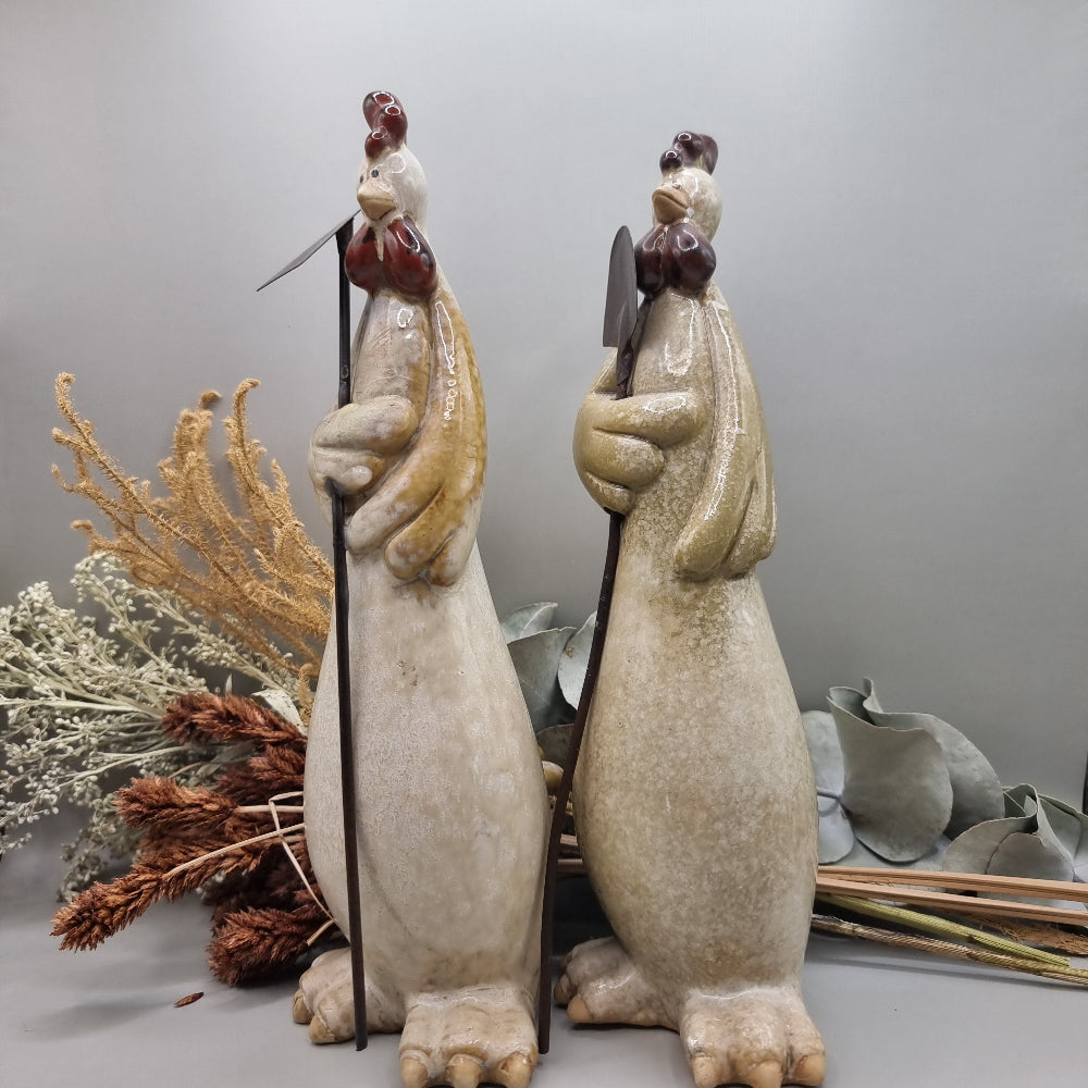 Tall ceramic rooster sculptures holding garden tools, rustic and whimsical style.