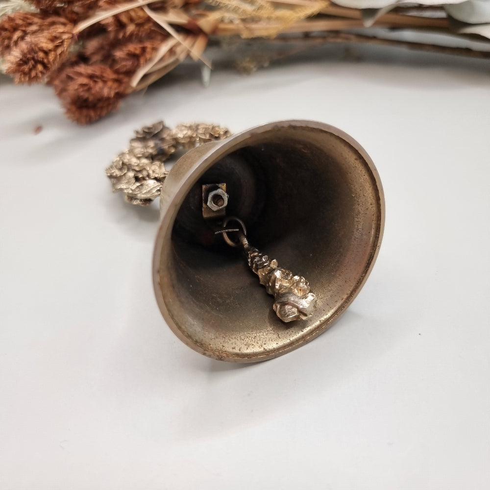 Vintage brass bell with rose wreath handle and aged patina.