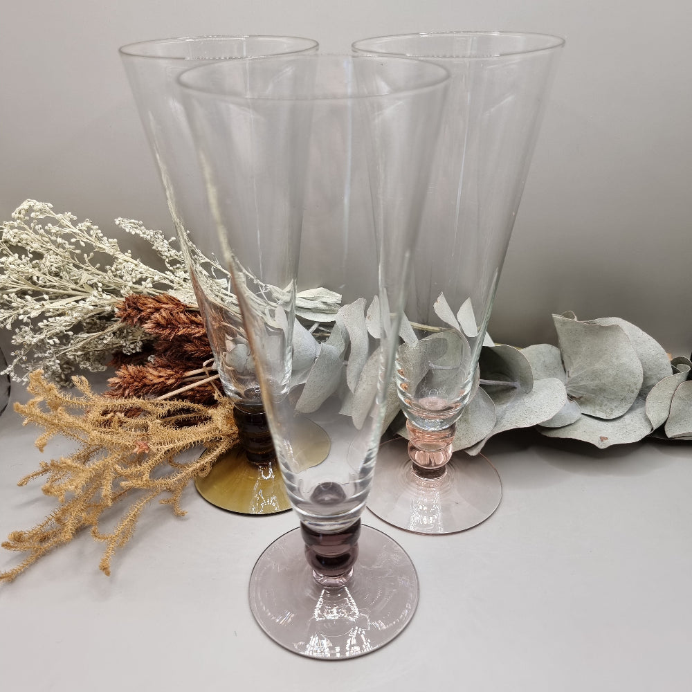 Set of three champagne flutes with pink, amber, and plum coloured bases