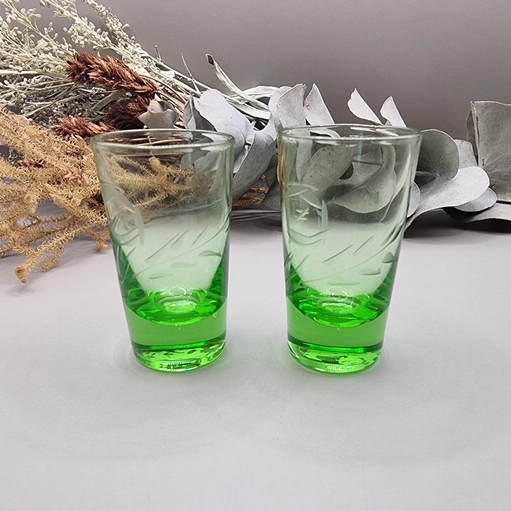 Pair of etched green glass shot glasses with clear tops and vibrant green bases.