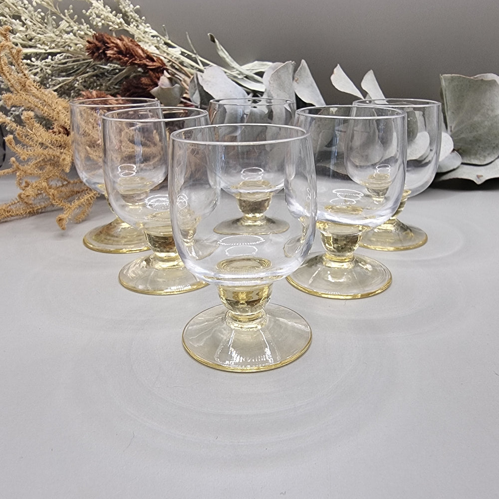 Set of six yellow-tinted vintage shot glasses with rounded bowls and short pedestal bases.
