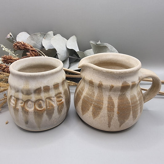 Stoneware jug and spoon holder with earthy feathered glaze in natural tones.