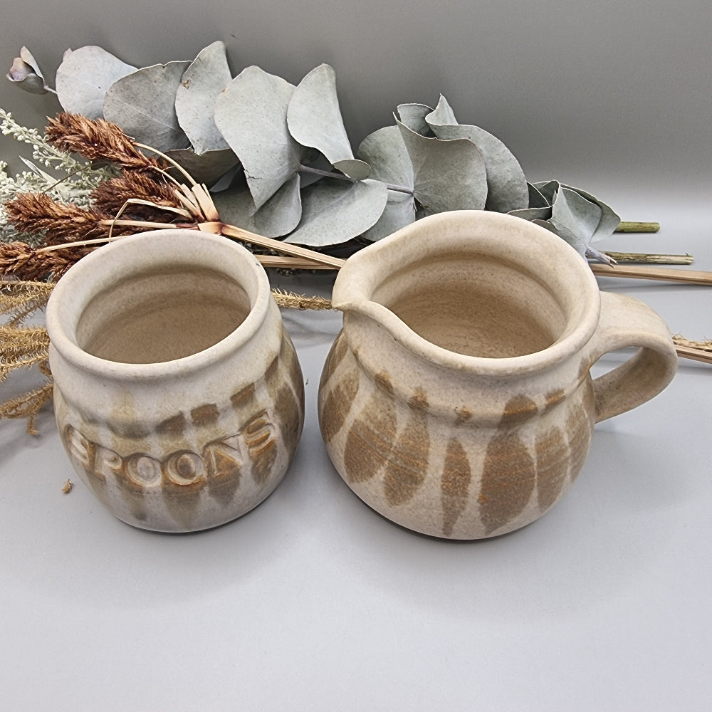 Stoneware jug and spoon holder with earthy feathered glaze in natural tones.