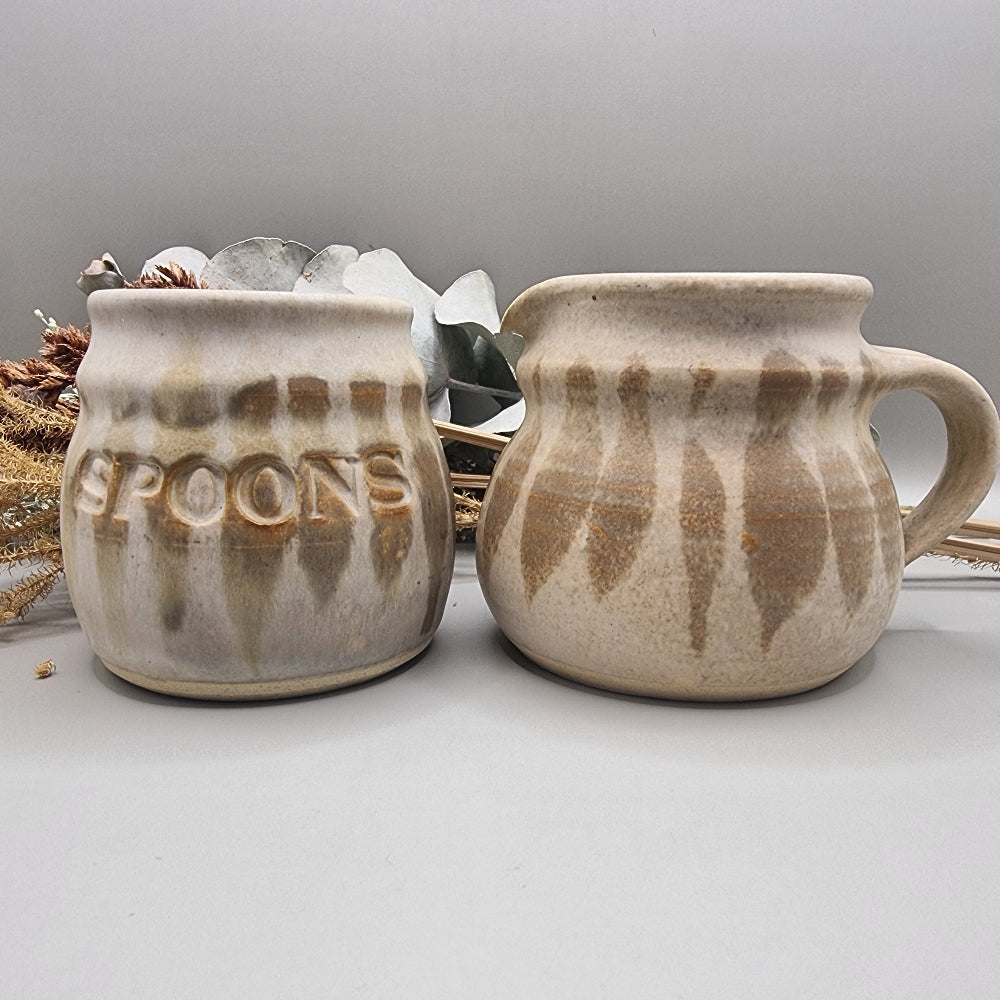 Stoneware jug and spoon holder with earthy feathered glaze in natural tones.