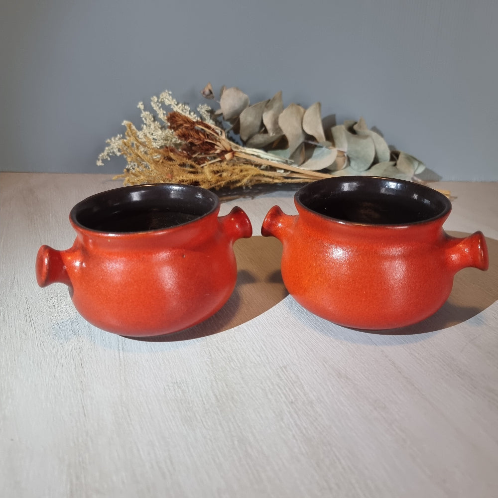 Pair of vintage red ceramic soup bowls with double handles and black interior.
