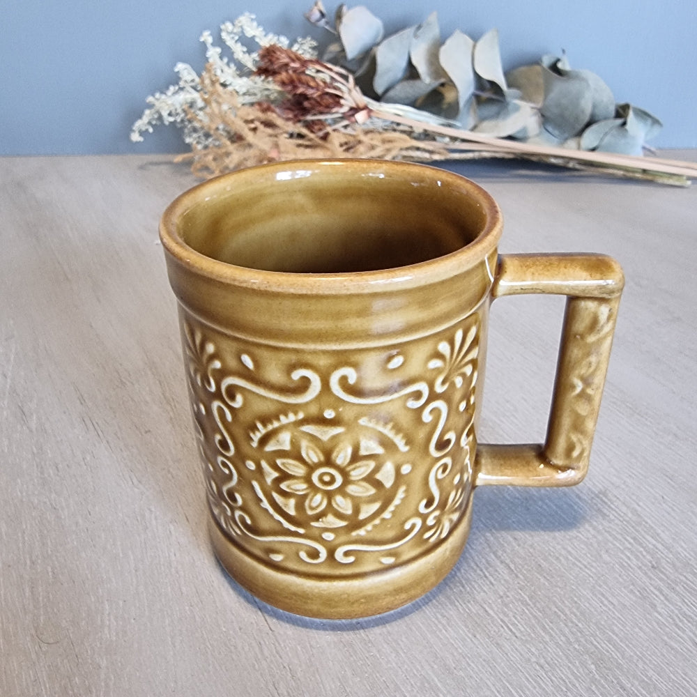 Crown Lynn embossed floral mug in caramel glaze with raised scroll and flower design.