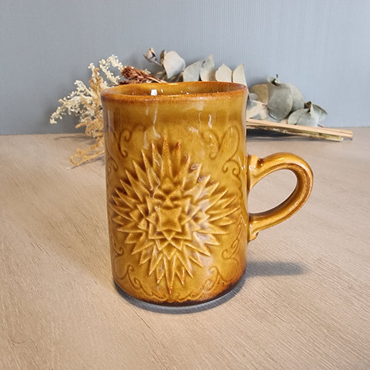Crown Lynn mug with embossed starburst design in golden-brown glaze.
