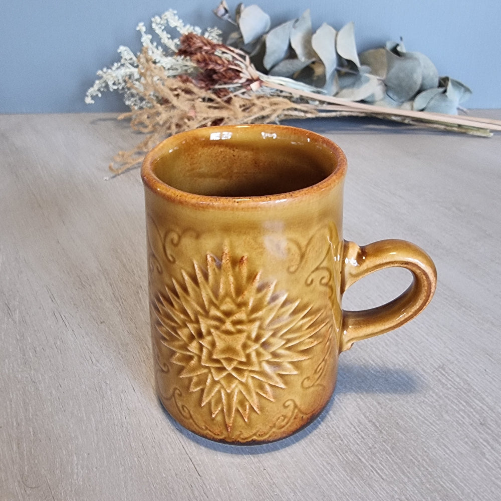 Crown Lynn mug with embossed starburst design in golden-brown glaze.