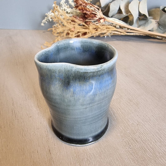 Handmade pottery cup with blue-grey glaze and organic shape, rustic and artistic.