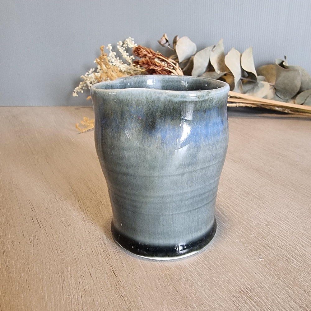 Handmade pottery cup with blue-grey glaze and organic shape, rustic and artistic.