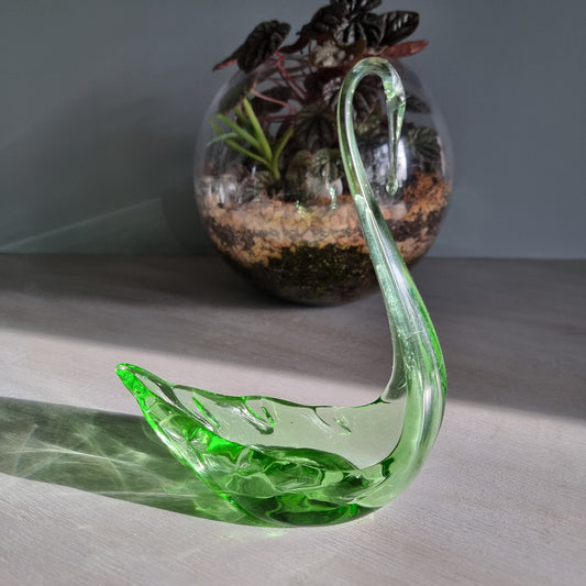 Vintage green art glass swan with curved neck catching the light on a table.
