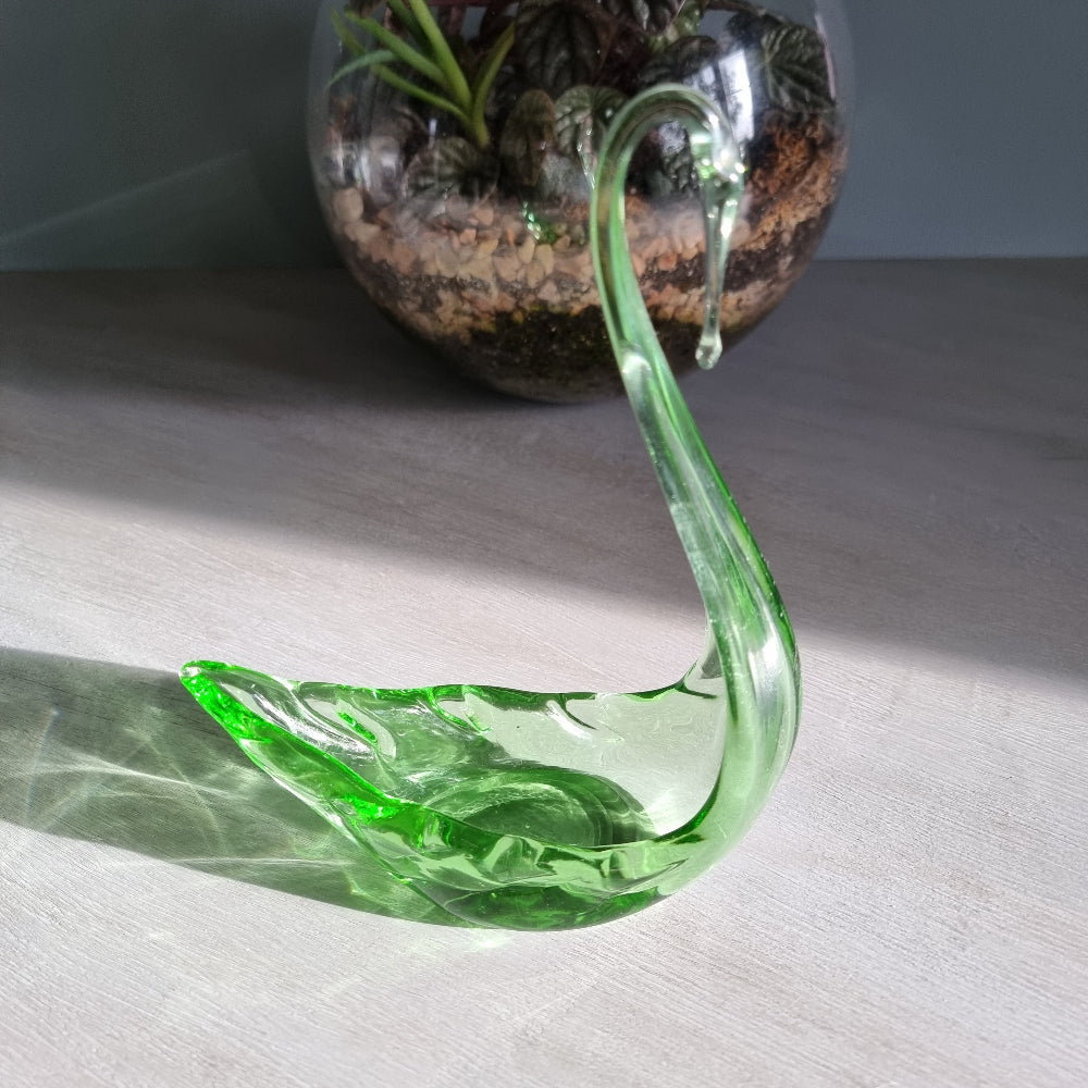 Vintage green art glass swan with curved neck catching the light on a table.