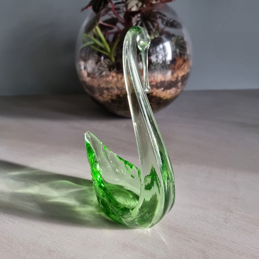 Vintage green art glass swan with curved neck catching the light on a table.
