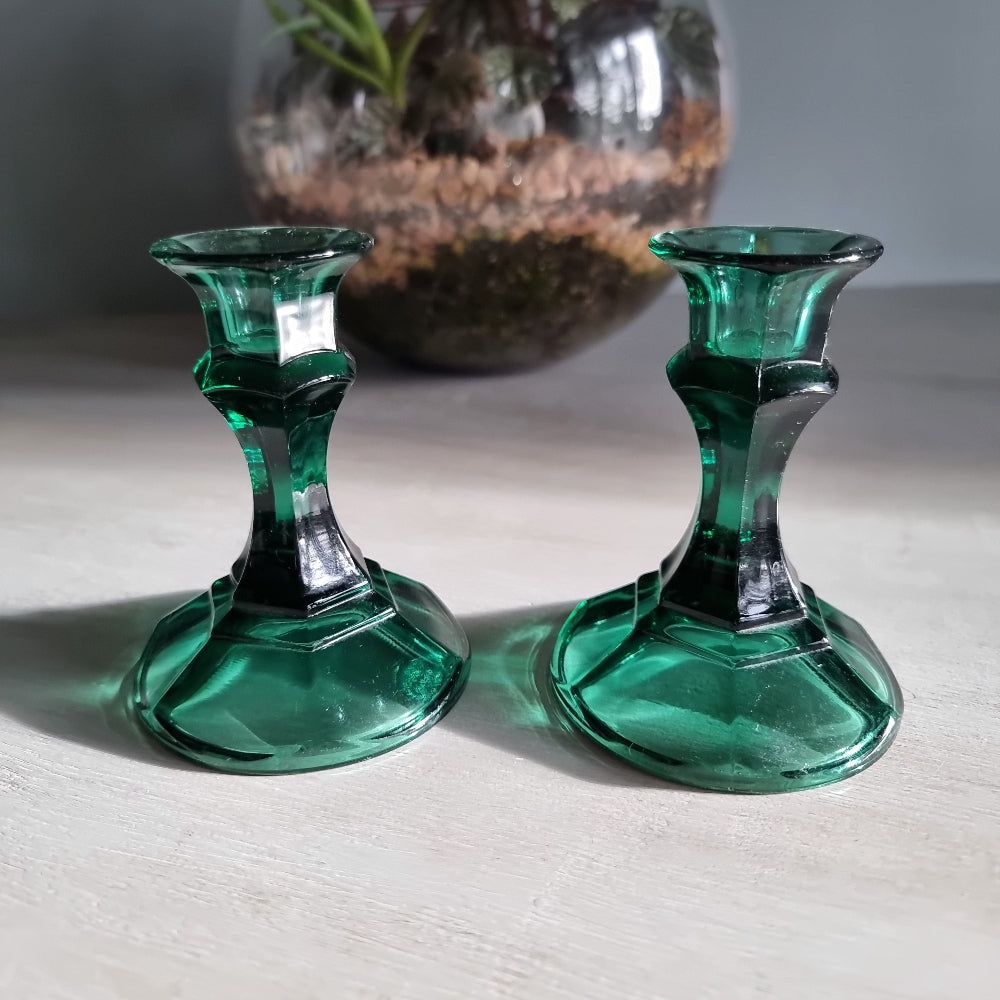 Pair of vintage emerald green glass candlestick holders catching light on a tabletop.