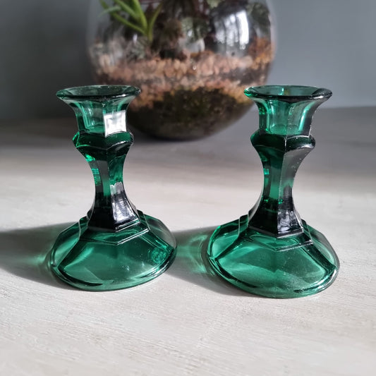 Pair of vintage emerald green glass candlestick holders catching light on a tabletop.